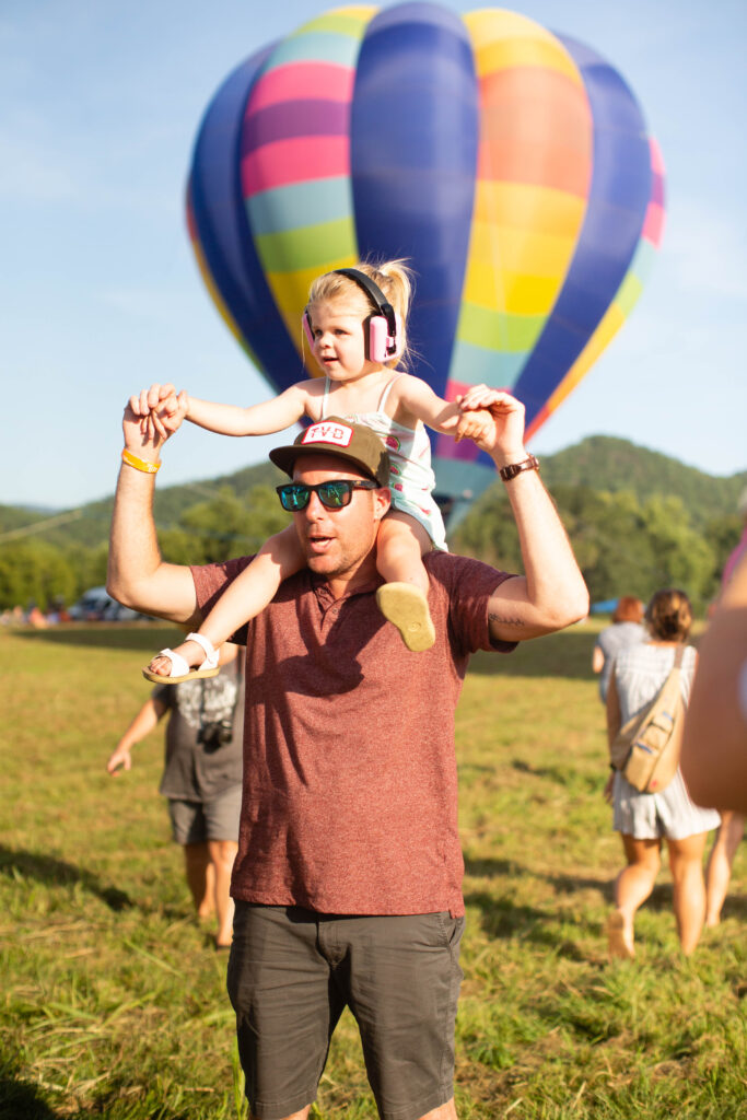 dad with daughter on his shoulders in front of hot air balloon
